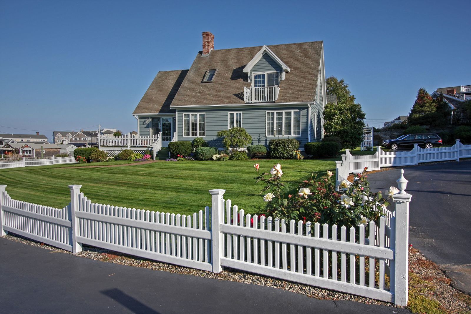 Cape Cod style house behind a white picket fence and roses